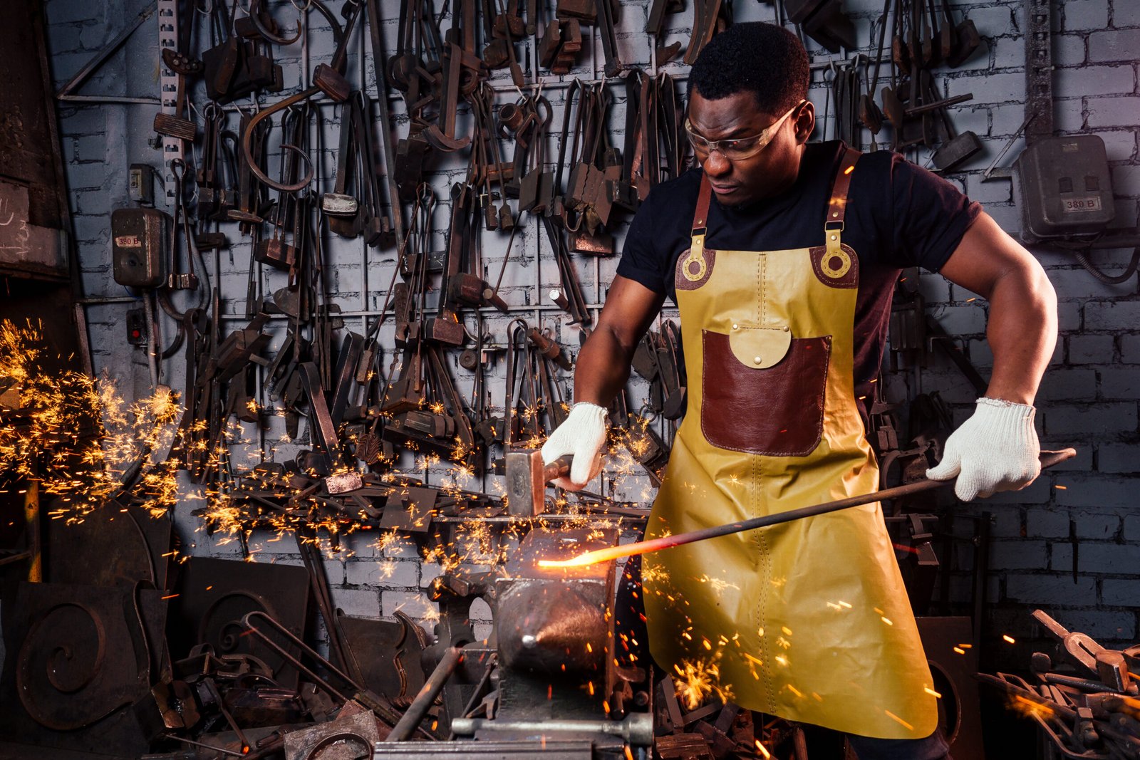 handsome african american blacksmith male worker working in workshop,wearing leather apron and protective glasses with gloves.concept save work.